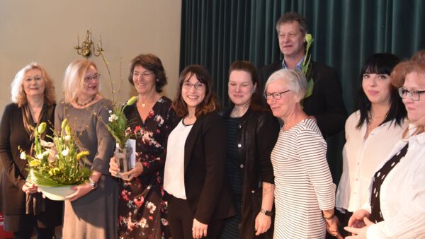 Mehrere lächelnde Personen. Einige haben Blumen in der Hand. Sechs Frauen und ein Mann dahinter.