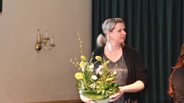 Eine Frau hält großes Blumengesteck in Glasschale in den Händen